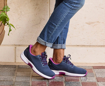 Navy blue running sneakers with purple collar and heel counter accents, on-model outdoor lifestyle shot showing engineered knit upper and white contrast midsole with pink outsole detail