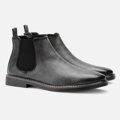 Black leather Chelsea boots with matching elastic side panels and grosgrain pull tabs, paired angled view featuring contrast white welt stitching and stacked heel detail
