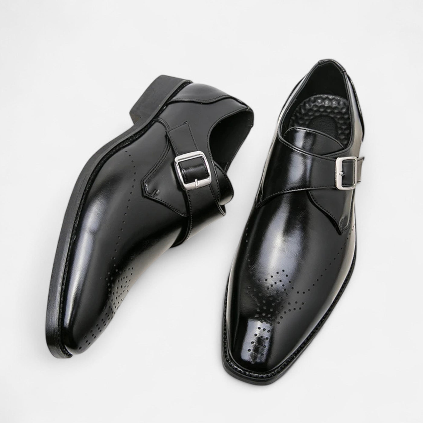 Black leather single monk strap dress shoes with brogue perforation detail and silver buckle closure, overhead paired view showing medallion toe cap and leather sole construction