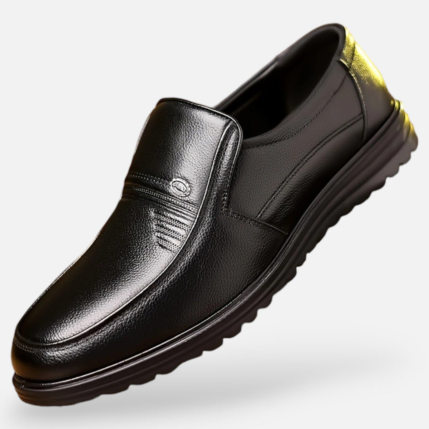 Black grain leather slip-on shoe with decorative stitching detail and metal badge embellishment, angled view showing thick ridged rubber comfort sole and yellow heel tab