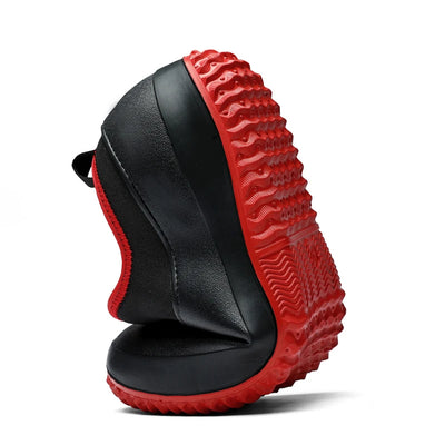 Black flexible slip-on shoe with red collar and red rubber outsole, dynamic flex view showing grooved sole construction and neoprene collar stretch detail