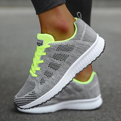 Grey mesh trainers with neon yellow laces and collar accents, on-model close-up displaying open mesh construction and white textured midsole with black rubber outsole

