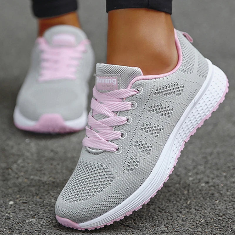 Grey knit athletic sneakers with pink flat laces and heel counter trim, on-model side view showing breathable mesh upper panels and white EVA midsole with pink traction sole