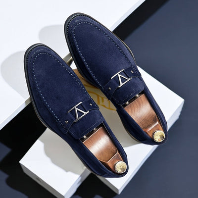 Navy blue suede loafers with silver metal ornament detail and studded strap, overhead paired view displaying contrast stitching and wooden shoe forms with brass caps