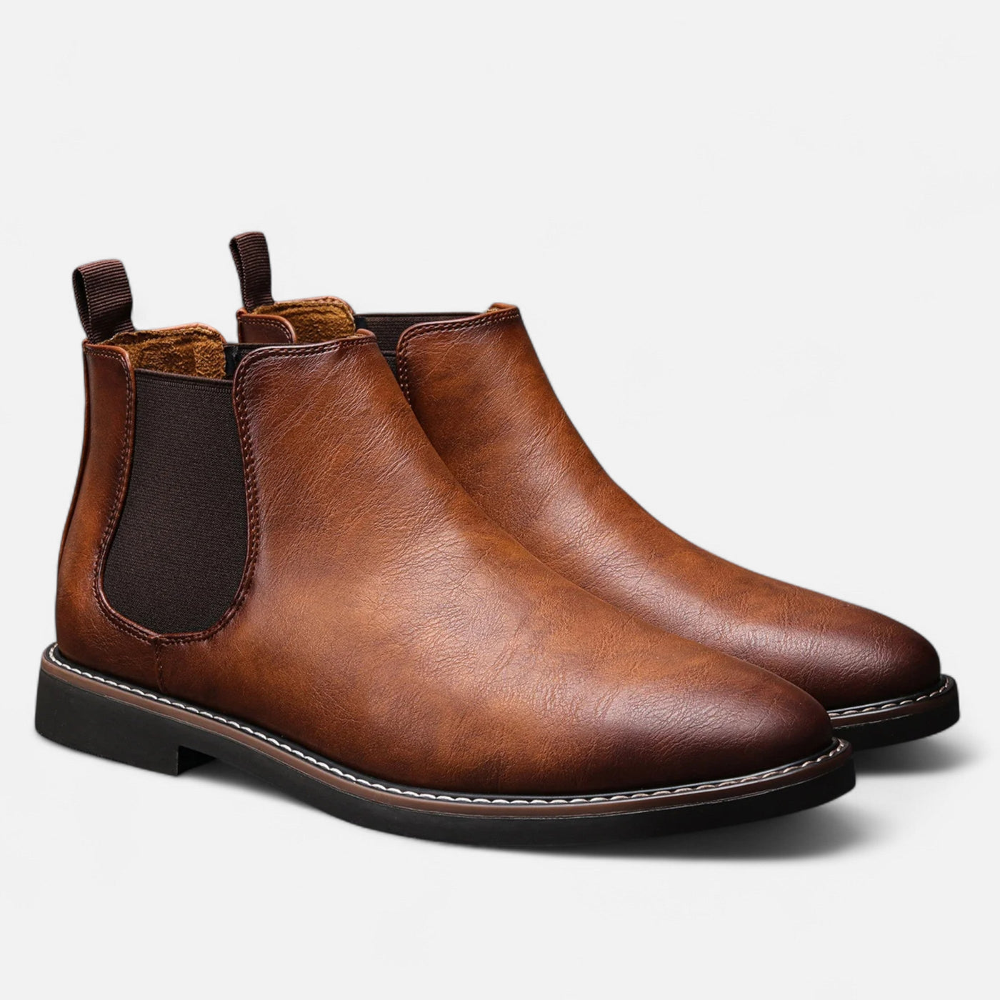 Tan cognac leather Chelsea boots with black elastic side gussets and pull tabs, paired three-quarter view showing contrast welt stitching and textured rubber sole